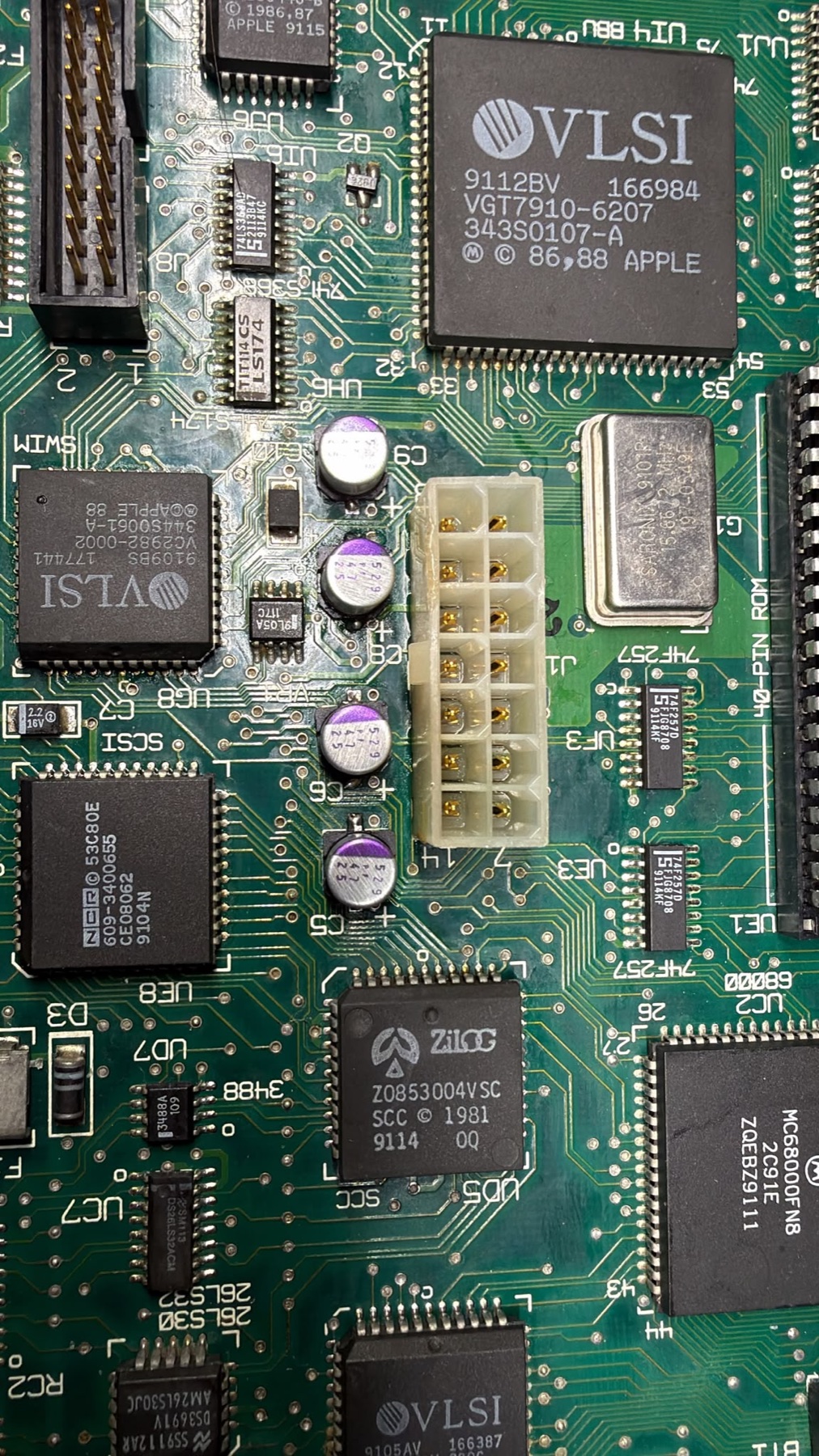 A close-up of the Macintosh Classic logic board with the first four purple-topped replacement capacitors installed